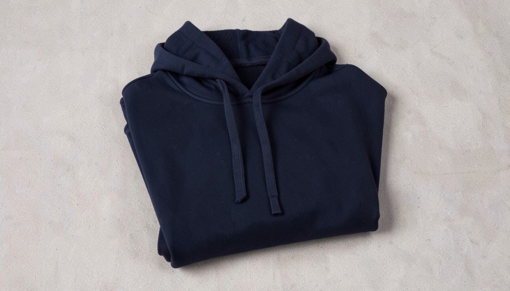 Folded navy blue hooded sweatshirt with drawstrings, placed on a light textured surface