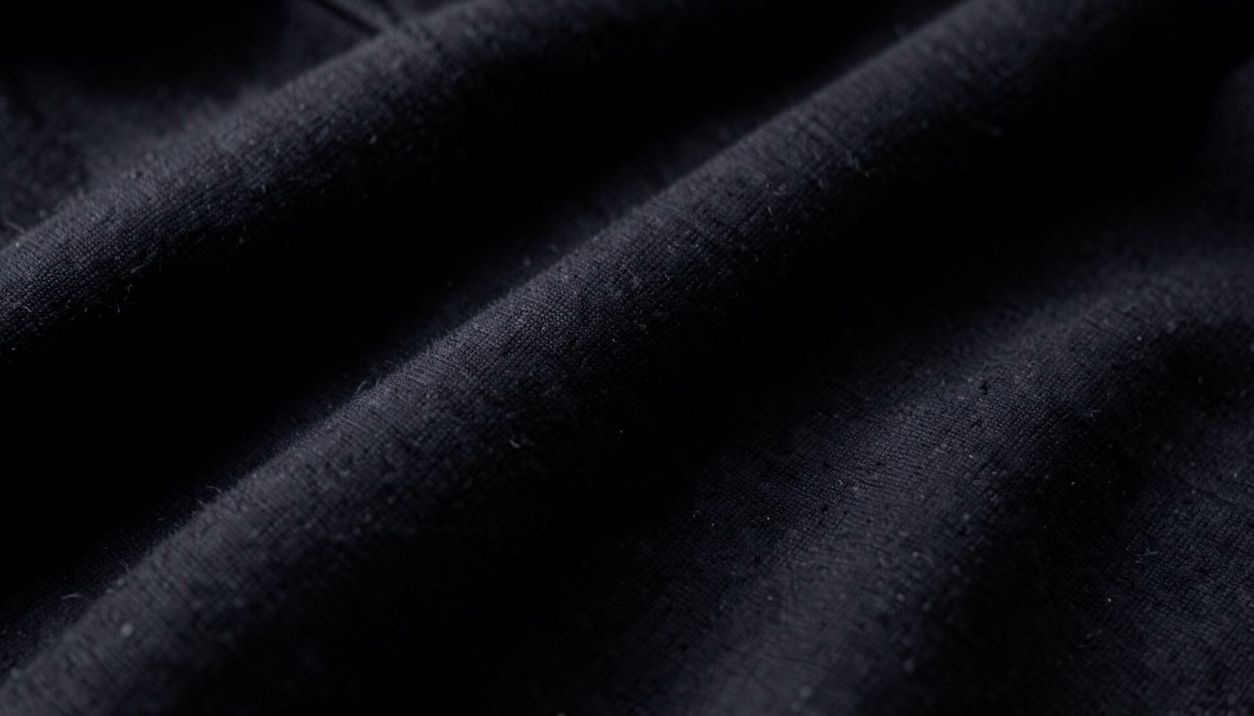 Close-up of dark folded fabric with visible weave texture, moody low-light shot